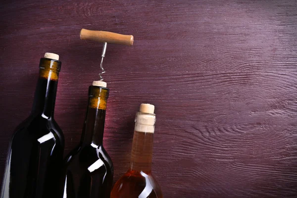 Drie fles wijn en kurkentrekker op paarse houten achtergrond — Stockfoto