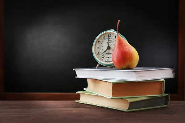 Birne und Uhr mit Büchern auf dem Schreibtisch — Stockfoto