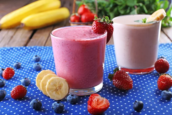 Vasos de batido frío fresco con frutas y bayas, sobre fondo de mantel azul —  Fotos de Stock