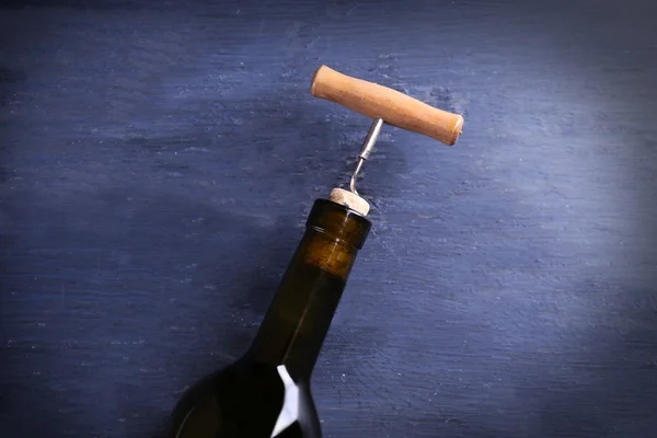 Corkscrew and wine bottle on blue wooden background — Stock Photo, Image