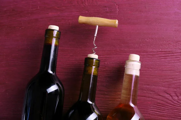 Tres botellas de vino y sacacorchos sobre fondo de madera púrpura —  Fotos de Stock