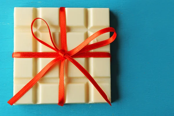 Barre de chocolat blanc avec noeud rouge sur fond en bois couleur — Photo