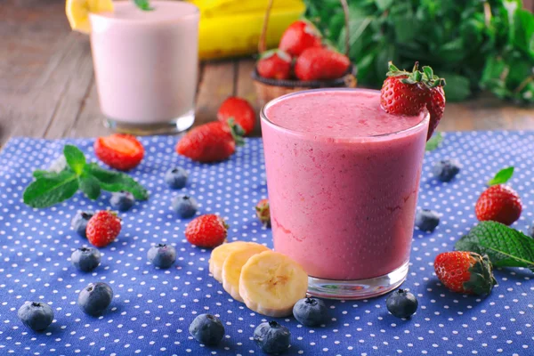 Vasos de batido frío fresco con frutas y bayas, sobre fondo de mantel azul —  Fotos de Stock