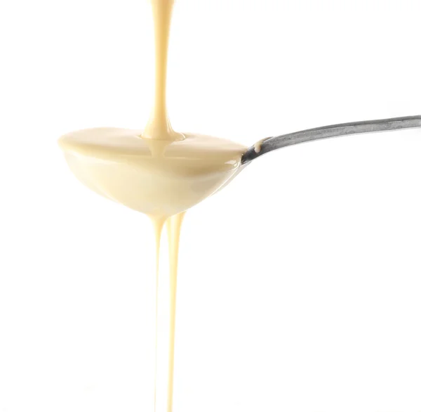 Condensed milk pouring from a spoon, isolated on white — Stock Photo, Image