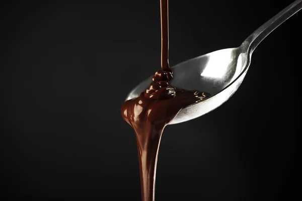 Chocolate poured on a spoon on dark background — Stock Photo, Image