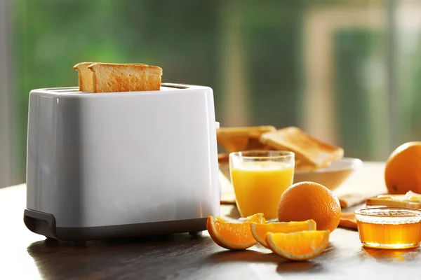 Mesa servida para café da manhã com torrada e suco de laranja, em fundo embaçado — Fotografia de Stock