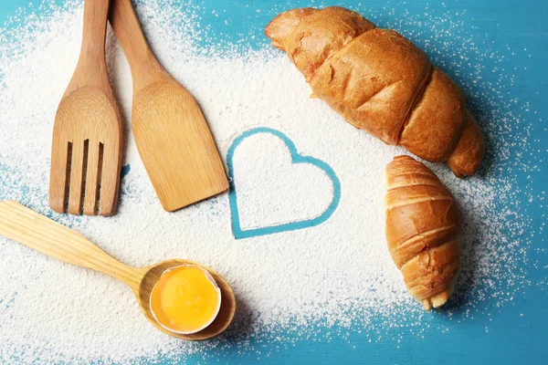 Heart of flour, croissant and  wooden kitchen utensils on color wooden background — Stock Photo, Image