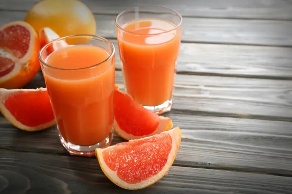 Sklenky grapefruitové šťávy a čerstvé ovoce na dřevěné pozadí — Stock fotografie