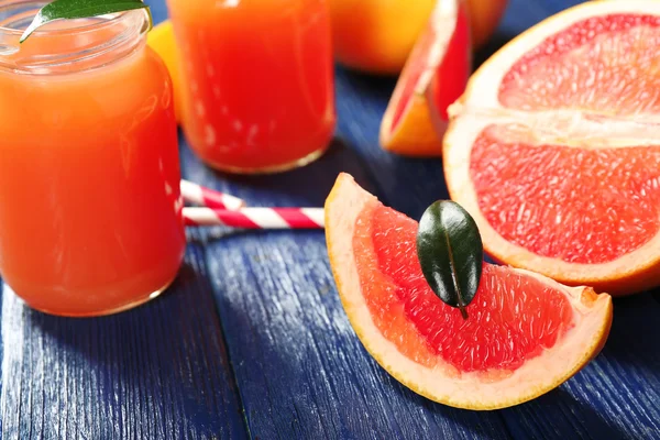 Grapefruitsaft in Flaschen und frisches Obst auf dunkelblauem Holzgrund — Stockfoto