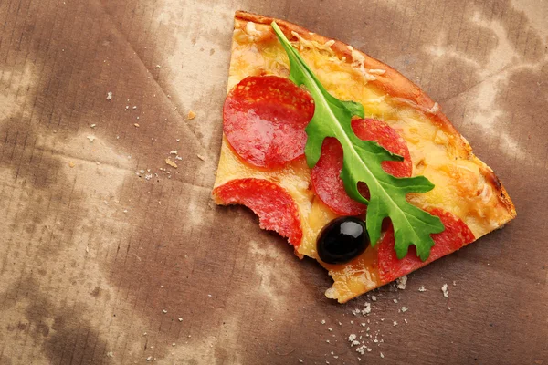 Fetta di pizza al salame piccante morsa con olive e rucola su cartone — Foto Stock