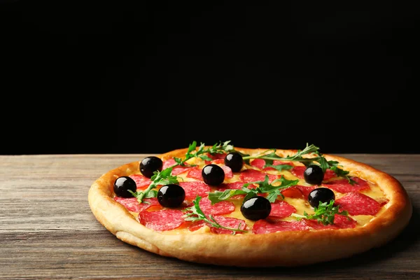 Tasty pizza with salami and olives on wooden table against black background — Stock Photo, Image