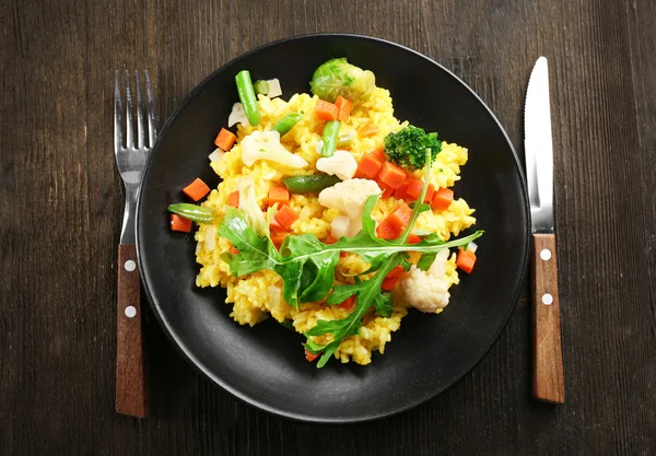 Svart plåt med vegetabiliska risotto, gaffel och kniv på träbord — Stockfoto