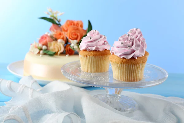Tasty cupcakes on stand and cake, on table, on color background — Stock Photo, Image