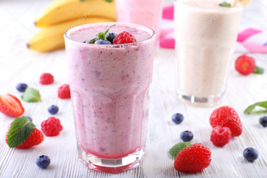 Milkshakes with berries on light wooden background
