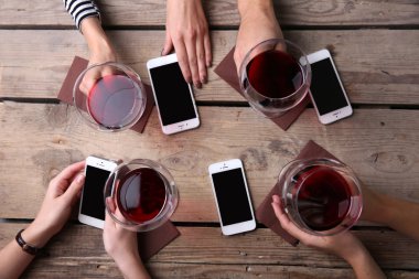 Kırmızı şarap, gözlüklü ahşap masa arka planda tutarak akıllı telefonlar ile dört el