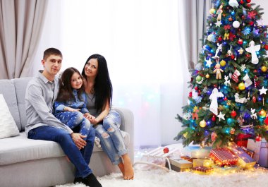Mutlu aile dekore edilmiş Noel odasında kanepede oturan