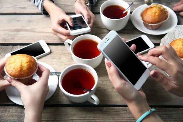 Quatre mains avec téléphones intelligents tenant tasses avec thé, sur fond de table en bois — Photo