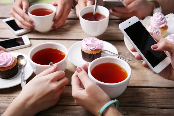 Quatre mains avec téléphones intelligents tenant tasses avec thé, sur fond de table en bois — Photo