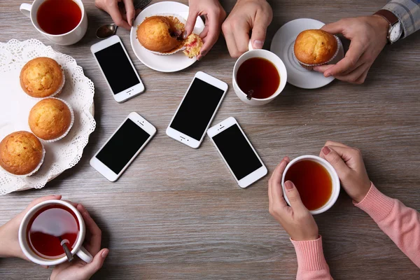 Quatre mains avec téléphones intelligents tenant tasses avec thé, sur fond de table en bois — Photo