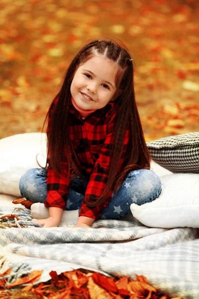 Gelukkig jong meisje, zittend op plaid in herfst park — Stockfoto