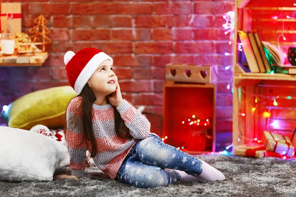 Hezká holčička v červeném klobouku sedí v vánoční zařízený pokoj — Stock fotografie