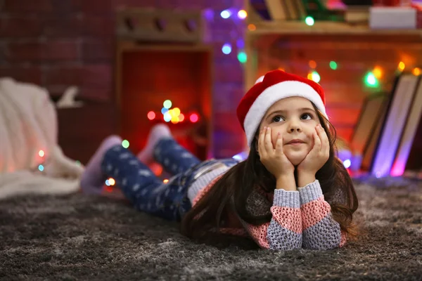 Hübsches kleines Mädchen mit rotem Hut legt in weihnachtlich dekorierten Raum — Stockfoto