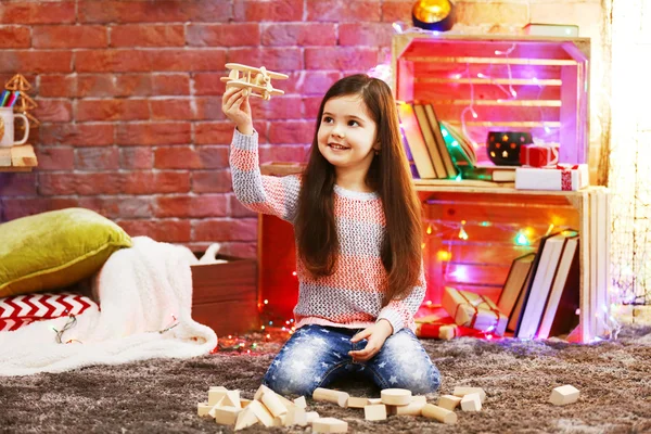 Hübsches kleines Mädchen spielt mit Holzflugzeug in weihnachtlich dekoriertem Zimmer — Stockfoto