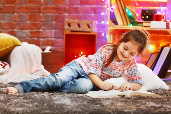 Hübsches kleines Mädchen mit Buch im weihnachtlich dekorierten Zimmer — Stockfoto