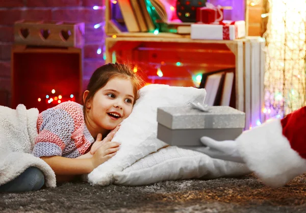 Bonita niña tendida en la almohada bajo una suave tela a cuadros esperando el regalo de Santa en la habitación decorada con Navidad — Foto de Stock