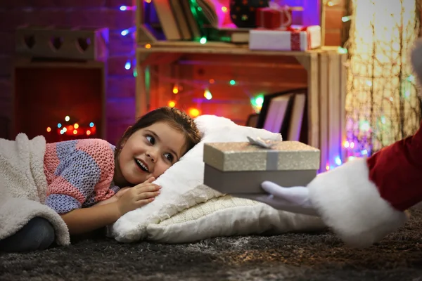 Bonita niña tendida en la almohada bajo una suave tela a cuadros esperando el regalo de Santa en la habitación decorada con Navidad — Foto de Stock