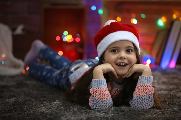 Hübsches kleines Mädchen mit rotem Hut legt in weihnachtlich dekorierten Raum — Stockfoto