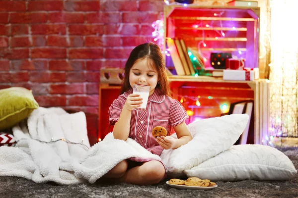 Hezká holčička s sklenici mléka a chutné cookies v vánoční zdobené místnosti — Stock fotografie