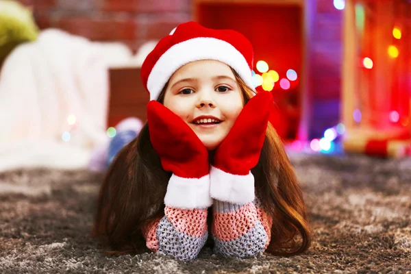 Menina bonita em chapéu vermelho e luvas que colocam no quarto decorado de Natal — Fotografia de Stock