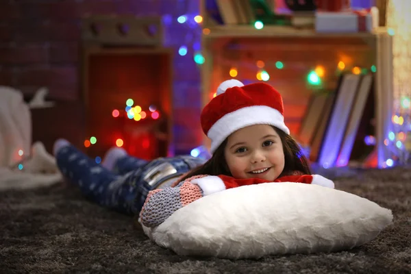 Söt liten tjej i röd hatt om på kudden i jul inrett rum — Stockfoto