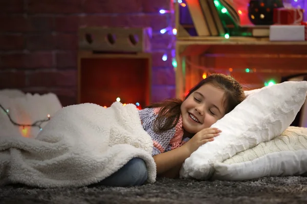 Bella bambina sdraiata sul cuscino sotto un morbido plaid nella stanza decorata di Natale — Foto Stock