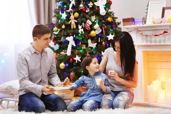 Familia feliz con leche y galletas dulces en la sala de Navidad decorada — Foto de Stock