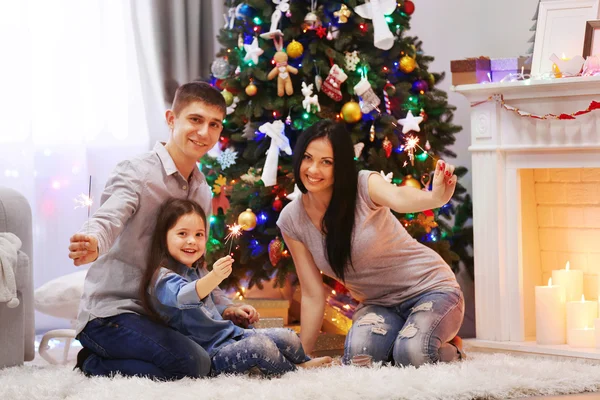 Joyeux famille avec des lumières du Bengale dans la salle de Noël décorée — Photo