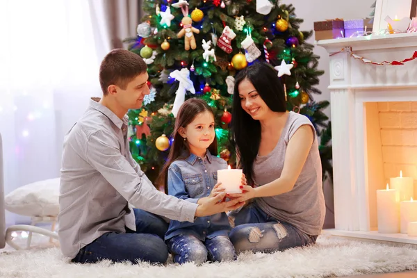 La familia feliz junta sostiene la vela en las manos en la habitación decorada de Navidad — Foto de Stock