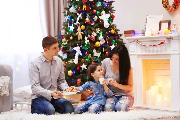 Familia feliz con leche y galletas dulces en la sala de Navidad decorada —  Fotos de Stock