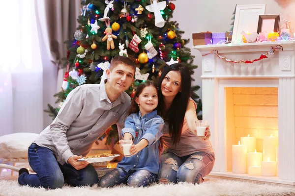 Famiglia felice con latte e biscotti dolci nella stanza decorata di Natale — Foto Stock
