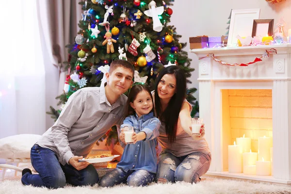 Famiglia felice con latte e biscotti dolci nella stanza decorata di Natale — Foto Stock