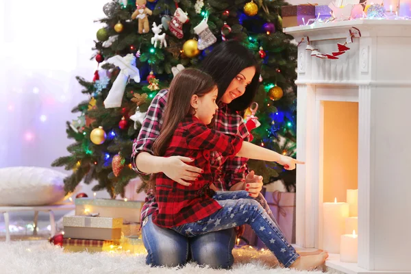 Mãe e filha felizes sentados perto de lareira decorativa no quarto — Fotografia de Stock