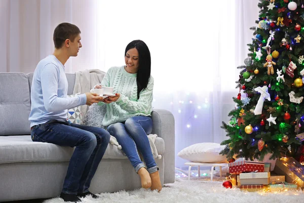 Pareja feliz sentada en el sofá en la habitación de Navidad decorada — Foto de Stock