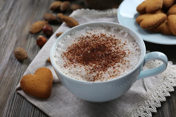 Secangkir coklat panas pada serbet kapas dengan kayu manis, almond dan kue berbentuk hati, tutup — Stok Foto