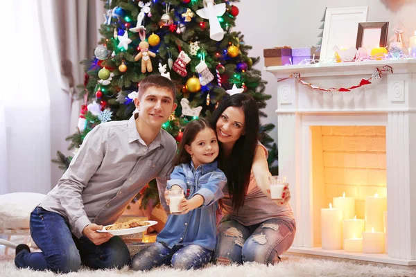 Happy family with milk and sweet cookies in the decorated Christmas room