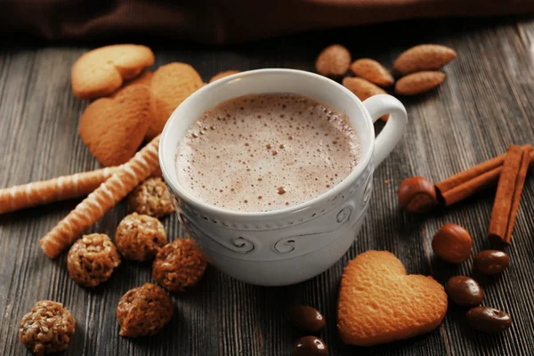 Cup of hot cacao with cinnamon, almonds and heart shaped cookies on wooden table — Stock Photo, Image