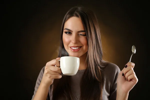 Mujer hermosa feliz con taza de café y cuchara sobre fondo oscuro — Foto de Stock