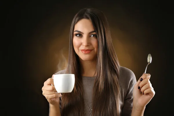 Happy krásná žena s šálkem kávy a lžíce na tmavém pozadí — Stock fotografie