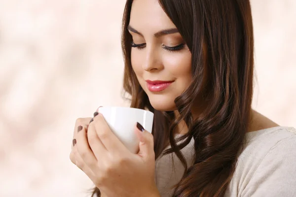 Portrait of young beautiful woman with cup of coffee on pink blurred background — Stock Photo, Image