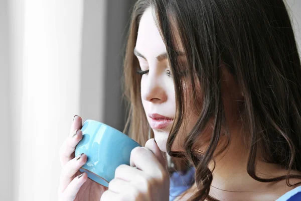 Frau mit Tasse Kaffee steht am Fenster im Zimmer — Stockfoto